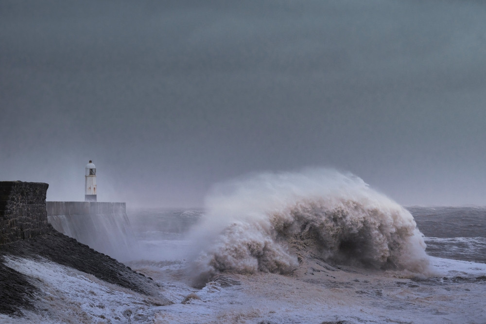 Une vague s'écrase sur une digue devant un phare