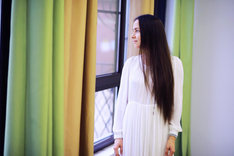 Une femme debout près d'une fenêtre avec des rideaux