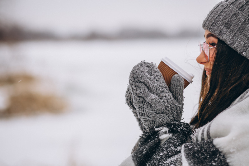 Une femme avec des gants boit une boisson chaude