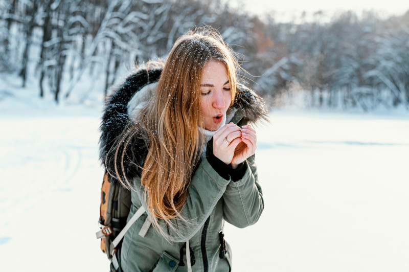 Une femme dehors souffle sur ses doigts en hiver
