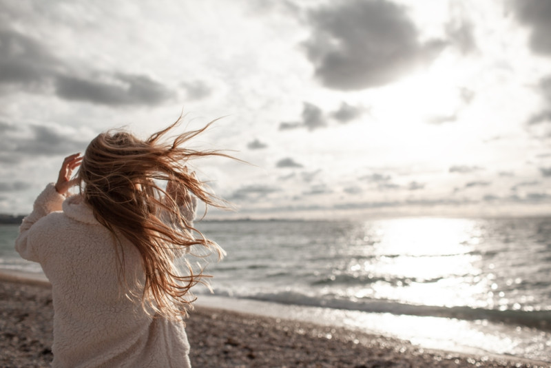 Une femme sur la plage face au vent