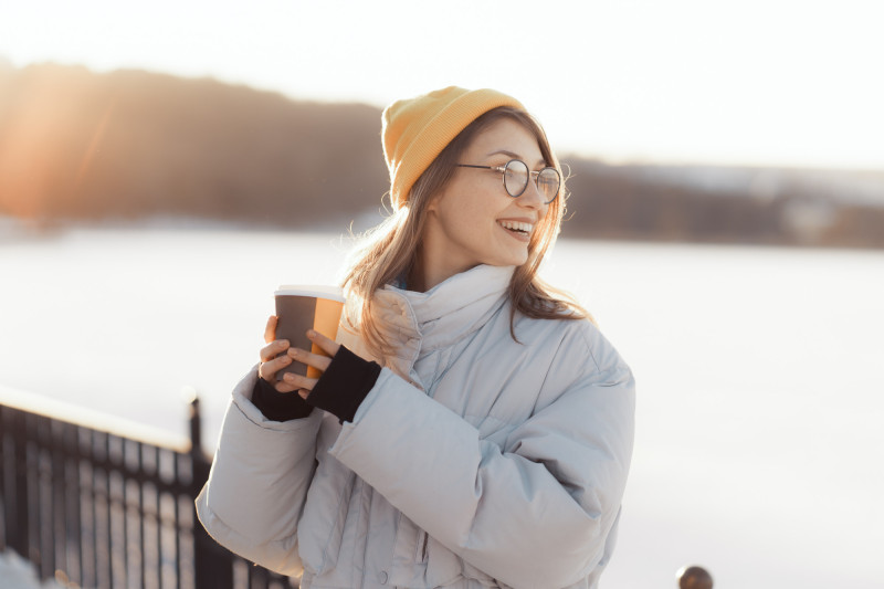 Une femme avec un bonnet dehors boit un café