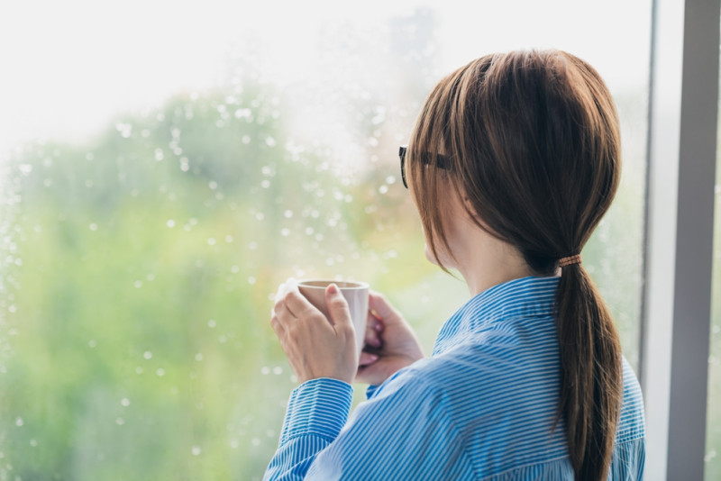 Une femme regarde par la fenêtre, il pleut