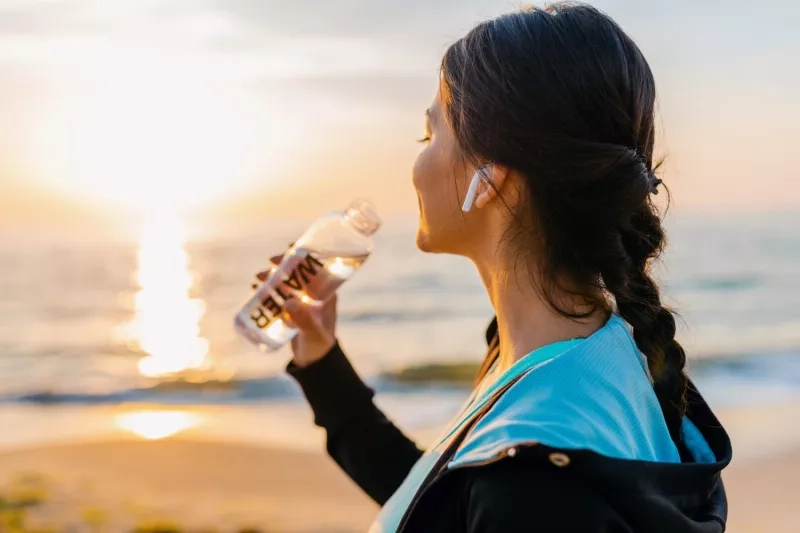 Femme sur la plage en train de boire de l'eau