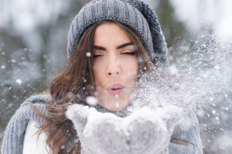 Femme qui souffle dans de la neige entre ses mains