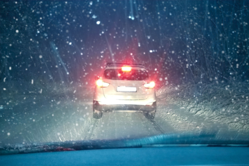 Une voiture roule de nuit dans la neige et le brouillard