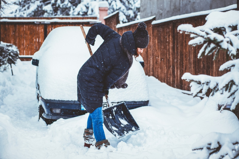 Une femme enlève la neige avec une pelle devant sa voiture
