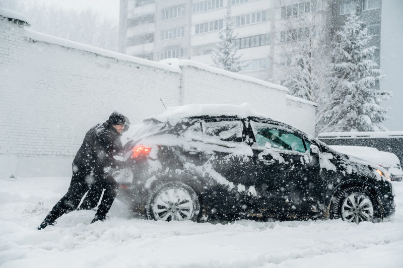 Un homme pousse sa voiture sous la neige