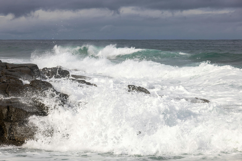 De puissantes vagues océaniques s'écrasent contre le rivage rocheux sous un ciel nuageux, révélant la beauté brute de la nature.