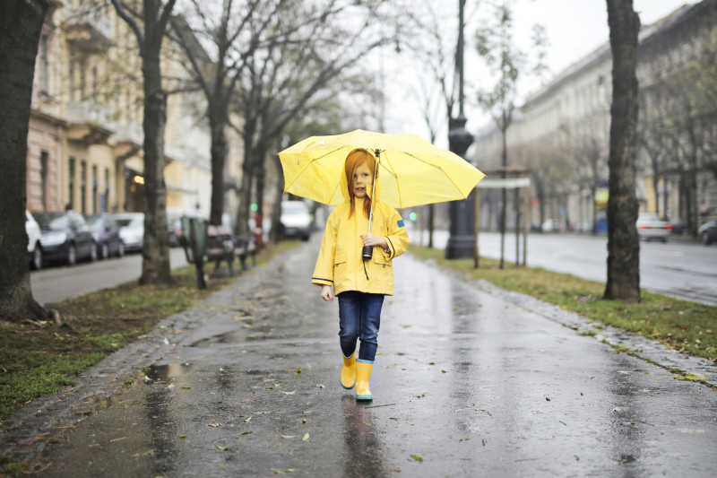 Fille En Imperméable Jaune Et Bottes Jaunes Tenant Un Parapluie Jaune Marchant Sur Une Promenade Latérale En Béton Gris
