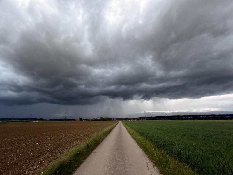 Des nuages ​​d'orage menaçants planent au-dessus d'un chemin de campagne et de champs dans la campagne suisse.