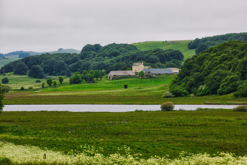 Paysage rural paisible en France, avec une ferme, des collines ondulantes et une rivière.