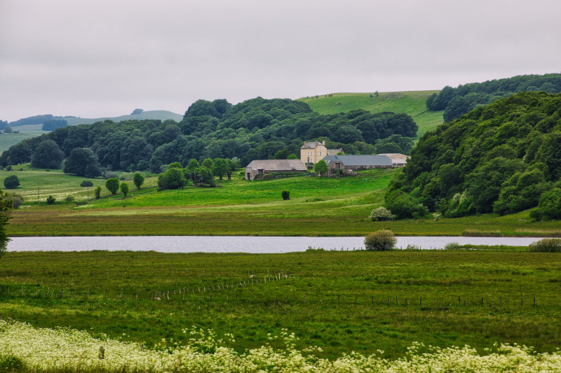 Paysage rural paisible en France, avec une ferme, des collines ondulantes et une rivière.