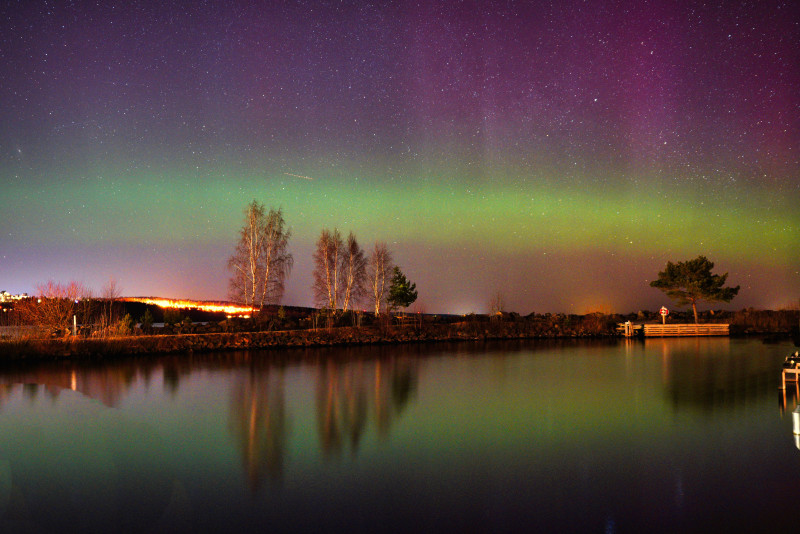 Une aurore boréale vibrante illumine le ciel nocturne au-dessus d'une scène tranquille au bord d'un lac.