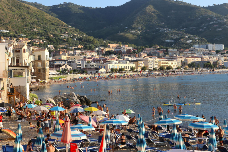 Journée d'été ensoleillée sur la plage de Cefalù, en Sicile, avec des baigneurs et un magnifique panorama côtier en toile de fond.