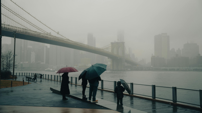 Des gens avec des parapluies regardant le pont de Brooklyn brumeux à New York.