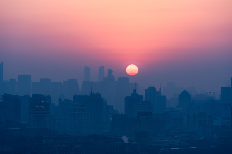 Silhouette d'une ville avec un coucher de soleil époustouflant, projetant une lueur chaleureuse sur les bâtiments.