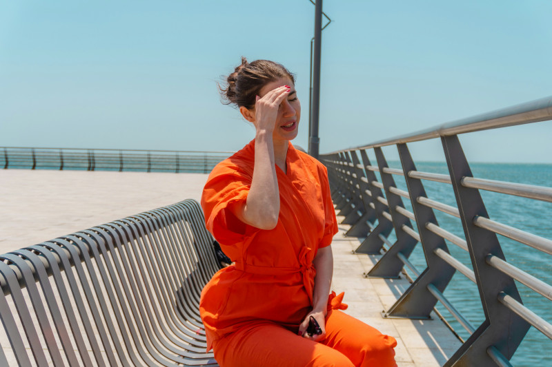 Woman in orange jumpsuit sits by the water.
