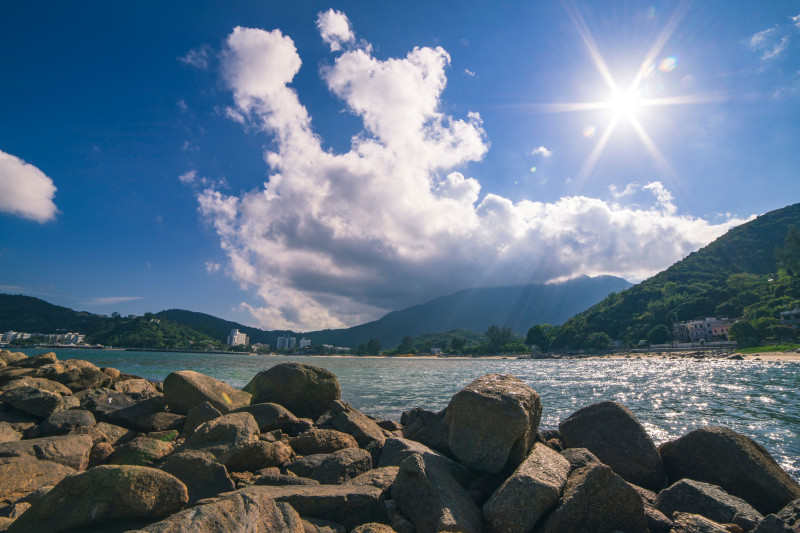 Vue côtière dramatique ensoleillée avec une côte rocheuse sous un ciel bleu clair et des nuages moelleux.