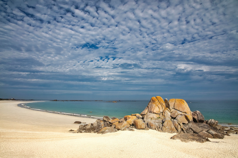 Belle plage de sable en Bretagne, France avec des formations rocheuses impressionnantes et une mer bleu clair.