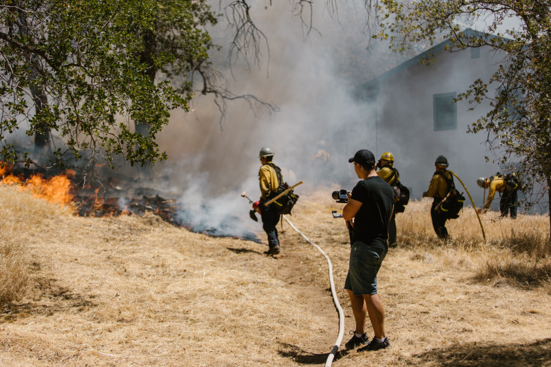 Des pompiers en tenue de protection luttent contre un incendie de forêt près d'une maison.