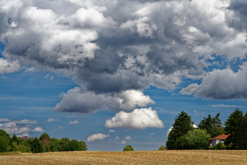 Un ciel nuageux vaste au-dessus d'un paysage rural serein avec des arbres et une maison lointaine.