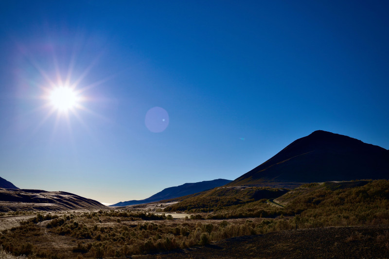 Paysage montagneux vibrant avec un soleil éclatant et un ciel bleu clair, capturant la beauté naturelle et la tranquillité.