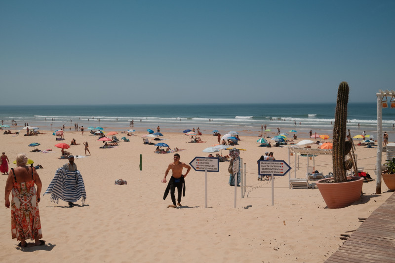Des personnes profitent d'une journée ensoleillée à la plage, sous des parasols colorés et un ciel d'un bleu limpide.