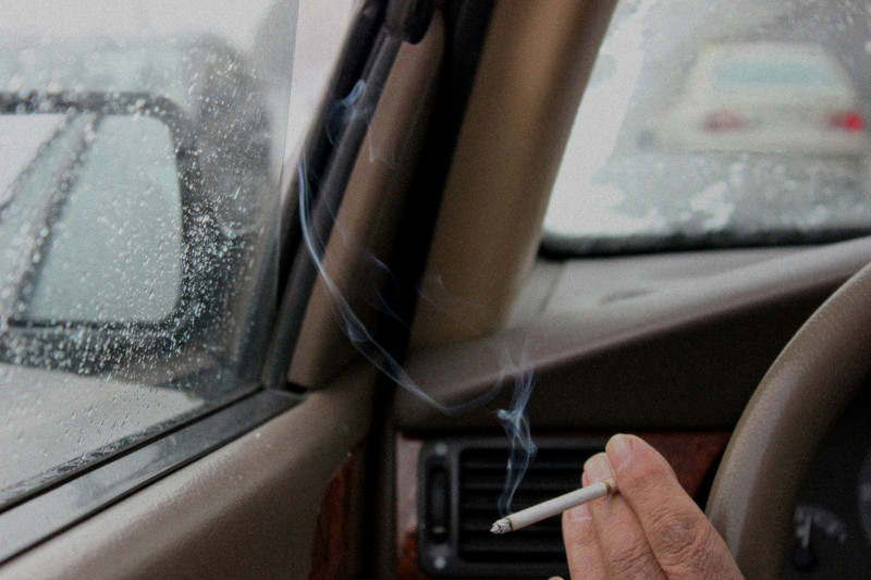A moody capture of a man smoking in a car on a rainy day, with raindrops trickling down the window.