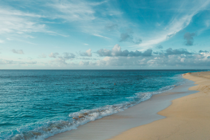 Paysage de plage serein avec un océan bleu clair et des nuages sous un ciel lumineux.