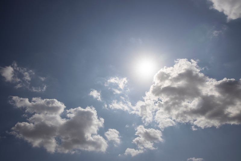 Un ciel bleu paisible avec des nuages blancs duveteux et un soleil éclatant, capturant une scène extérieure sereine.