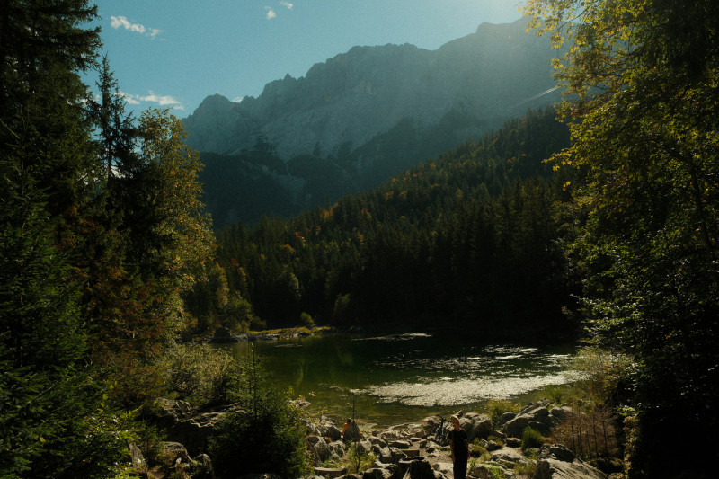 Sunlit lake surrounded by forest and mountains.