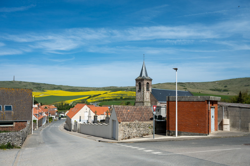 Scène de village à Escalles, Hauts-de-France avec un ciel bleu clair et un paysage rural.