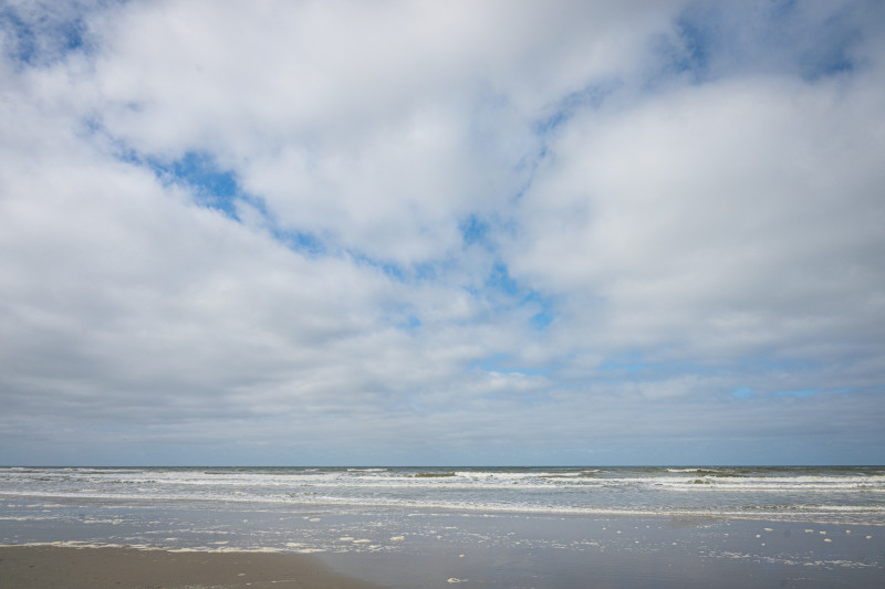 A sandy beach with ocean waves under a cloudy sky.