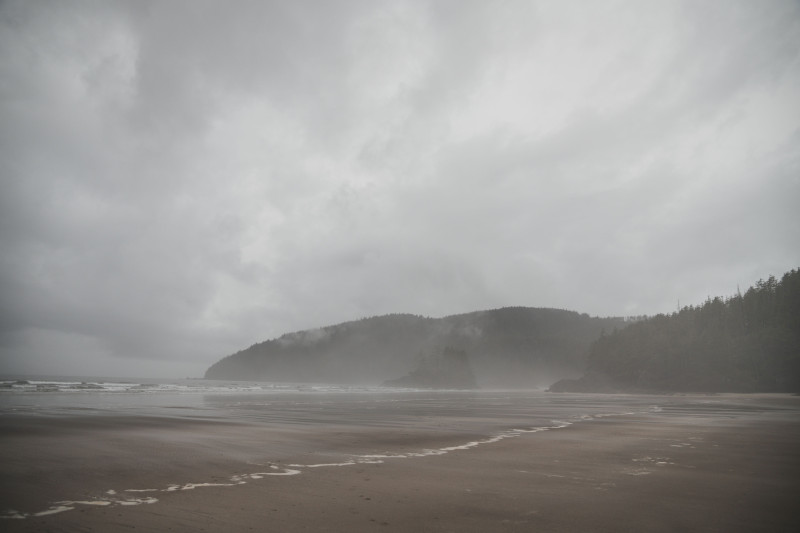 Une plage sereine avec des collines embrumées sous un ciel nuageux, mettant en valeur la côte océanique tranquille.