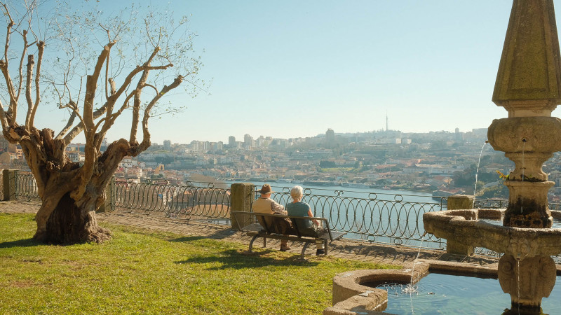 Une scène sereine : un couple de personnes âgées assis sur un banc, surplombant le fleuve et la ville de Porto.