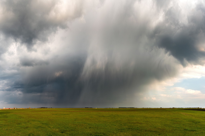 Des nuages orageux majestueux se forment au-dessus d'un vaste champ de gazon, annonçant une pluie imminente.