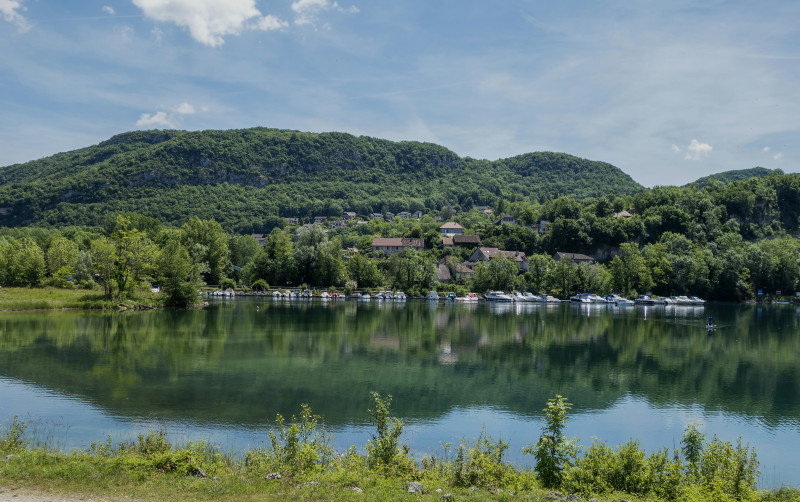 Un village tranquille s’étend le long des rives du Rhône, ses maisons bordant un plan d’eau paisible entouré de collines verdoyantes. Ce paysage typique du sud-est de la France évoque la douceur de vivre, entre nature généreuse et charme rural. Une scène 