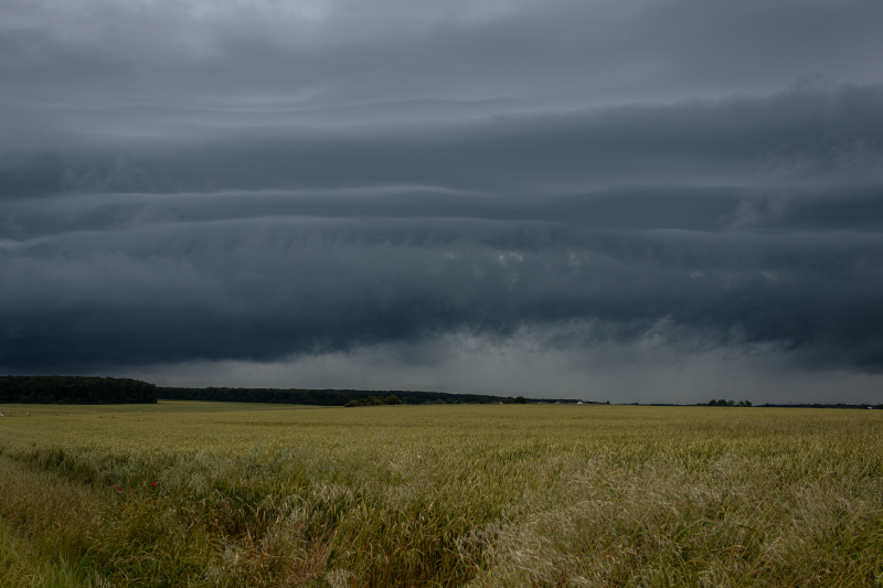 De sombres nuages ​​d'orage s'amoncellent au-dessus d'un vaste paysage rural, créant un ciel spectaculaire.