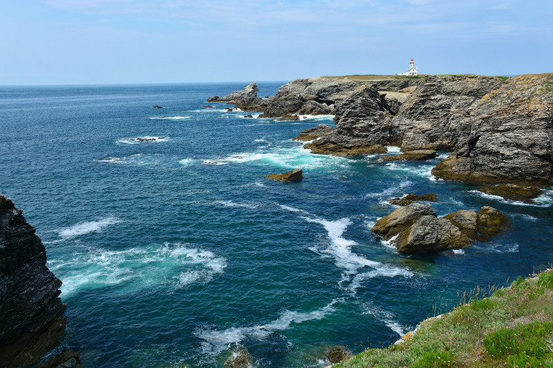 Éblouissantes falaises côtières et phare à Pointe des Poulains, Bretagne sous un ciel bleu clair.