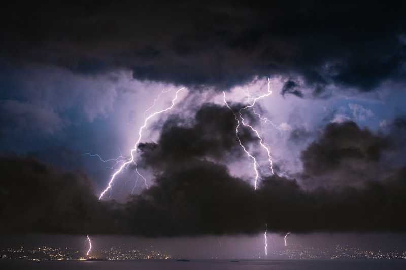 Bright lightning bolts striking behind dark storm clouds over a distant city skyline