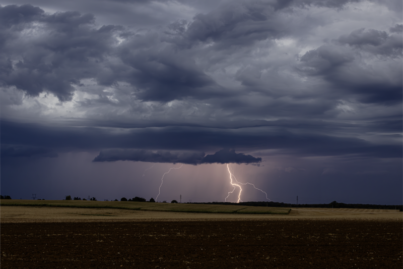 Des éclairs illuminent un ciel sombre et orageux au-dessus d'un paysage rural français.