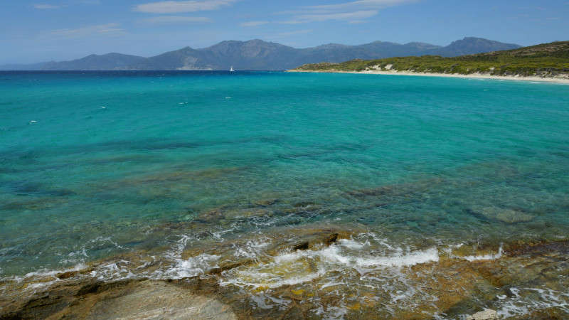 Turquoise ocean waves breaking on rocks with distant mountains