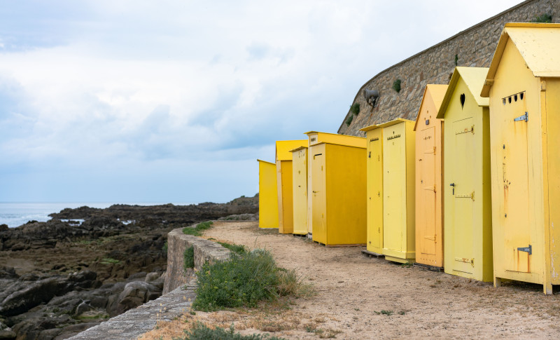 Des cabines de plage jaunes vives bordent la côte rocheuse de Batz-sur-Mer, France.