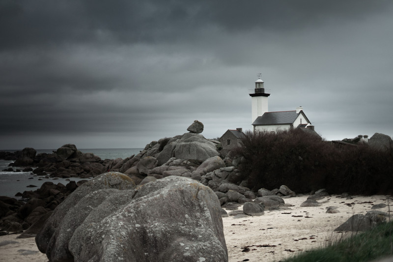 Vue pittoresque d'un phare sur la côte rocheuse de Bretagne sous un ciel orageux, France.