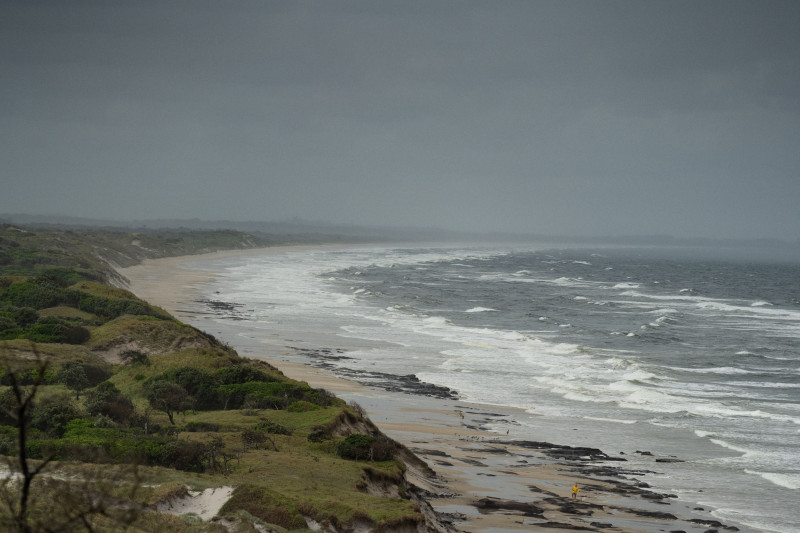 Vue aérienne d'une côte tempétueuse avec des vagues s'écrasant sur la plage et un ciel nuageux.