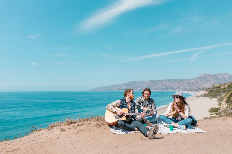 Trois amis assis sur une couverture de pique-nique au bord de l'océan, profitant de la musique et de la camaraderie.