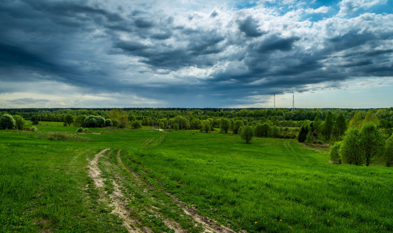 Paysage rural pittoresque avec des nuages dramatiques et des champs verdoyants sous un ciel nuageux.