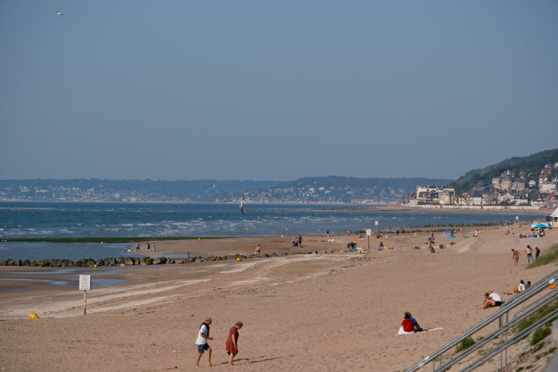 Des visiteurs profitent d'une journée ensoleillée à la plage de Cabourg en Normandie, France, avec un ciel dégagé et des vagues calmes.