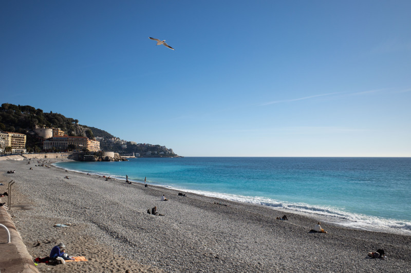 Plage paisible avec des eaux d'un bleu vibrant et des personnes se relaxant sous le ciel d'été clair à Nice, France.